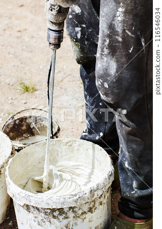 Adhesive mortar mix for tiling, builder uses paddle attachment for electric drill and bucket. 116546034