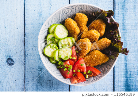 Close up of bowl with crispy nuggets, tomato and cucumber on the table top view 116546199