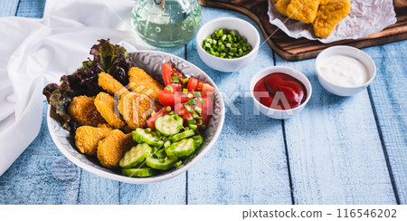 Bowl with crispy nuggets, tomato and cucumber on the table web banner 116546202