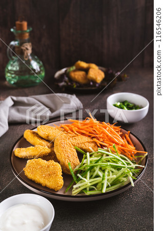 Chicken nuggets, grated cucumber and carrots on a plate on the table vertical view 116546206