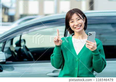 Smiling woman holding a smartphone in front of a car Smartphone and car 116546479