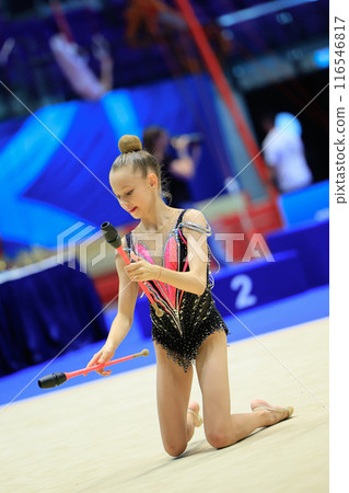 A young rhythmic gymnast shows agility and artistry performing with clubs on a competitive stage A young rhythmic gymnast shows agility and artistry performing with clubs on a competitive stage 116546817