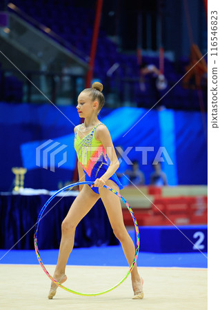 A young rhythmic gymnast shows her hoop skills at a lively competition in an indoor arena A young rhythmic gymnast shows her hoop skills at a lively competition in an indoor arena 116546823