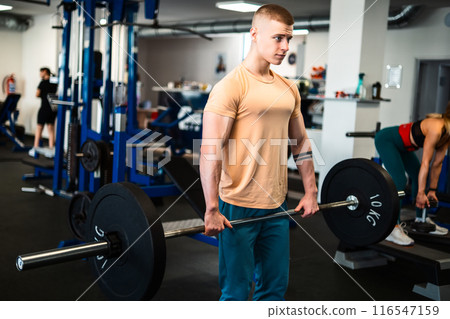 A male bodybuilder performs a weightlifting exercise in a gym 116547159