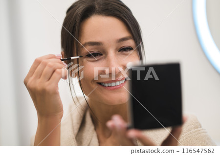 Cute dark-haired young woman doing her make up and looking contented 116547562