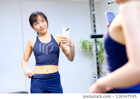 Young woman taking a picture of her abs with her smartphone at a sports gym, personal gym, muscle training girl, private room, selfie Young woman taking a picture of her abs with her smartphone at a sports gym, personal gym, muscle training girl, private room, selfie 116547595