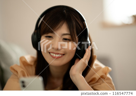 A middle-aged woman lying on a sofa listening to music on her smartphone A middle-aged woman lying on a sofa listening to music on her smartphone 116547774