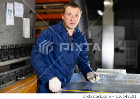 Positive worker marking metal sheet with tape measure in workshop 116548191
