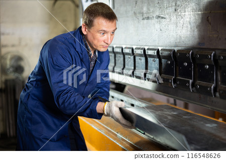 Worker placing metal sheet on bending machine in workshop 116548626