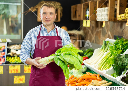 Male employee was distracted for minute and stands smiling with crisp lettuce in hands Male employee was distracted for minute and stands smiling with crisp lettuce in hands 116548714
