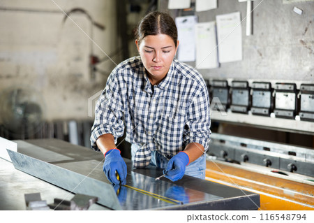 Woman measuring sheet of metal with tape measure Woman measuring sheet of metal with tape measure 116548794