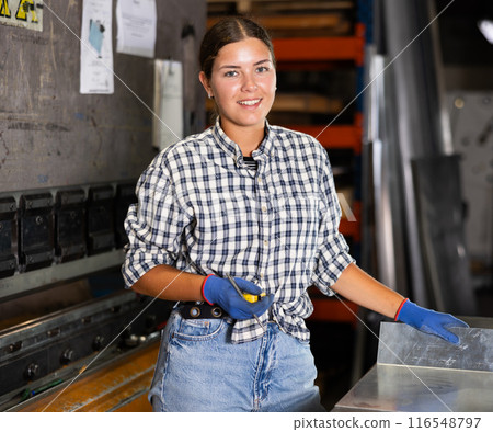 Female worker posing in metalworking shop with tape measure in hands Female worker posing in metalworking shop with tape measure in hands 116548797