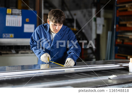 Guy measuring sheet of metal with tape measure 116548818