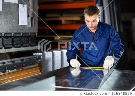 Man measuring sheet of metal with tape measure 116548839