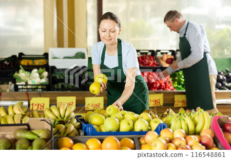 Smiling saleswoman laying out apples on counter in supermarket 116548861