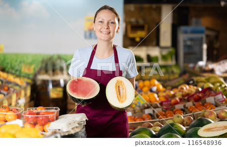 Woman seller in apron holds in watermelon and one-half melon packed in film Woman seller in apron holds in watermelon and one-half melon packed in film 116548936