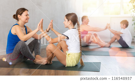 Woman practicing yoga in pair with her teen daughter during family workout at gym Woman practicing yoga in pair with her teen daughter during family workout at gym 116548937