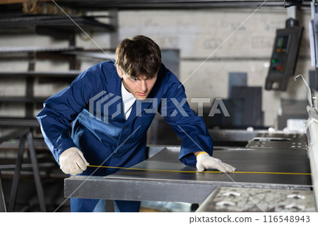 Young technician measuring steel sheet in metalworking workshop 116548943