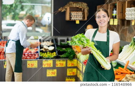 Young female seller in apron displaying assortment of celery at supermarket 116548966