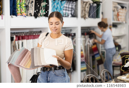Girl scrutinizes examine collection of samples of sheathing fabric in furniture store Girl scrutinizes examine collection of samples of sheathing fabric in furniture store 116548983