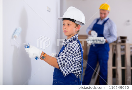 Boy painting wall with roller during repair works in apartment Boy painting wall with roller during repair works in apartment 116549050