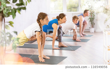 Pleasant preteen girl practicing variation of warrior pose of yoga with her family 116549056