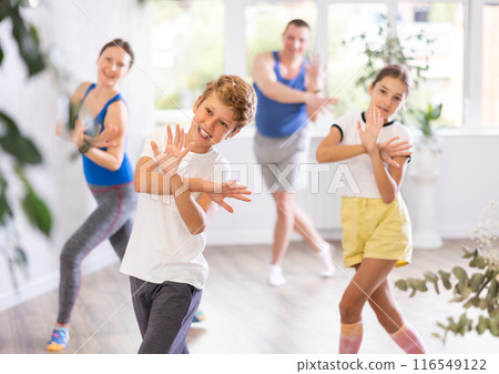 Happy sister and brother and their mom and dad practicing modern teen dance with crossed hands while training together in wellness center Happy sister and brother and their mom and dad practicing modern teen dance with crossed hands while training together in wellness center 116549122
