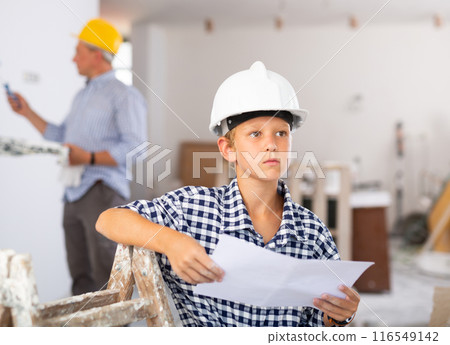 Portrait of builder boy checking blueprints in room being renovated 116549142