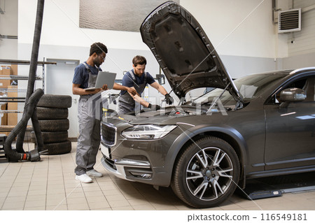 Two auto mechanics inspecting car engine in workshop Two auto mechanics inspecting car engine in workshop 116549181