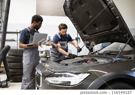 Two mechanics working on car engine with laptop in garage Two mechanics working on car engine with laptop in garage 116549187