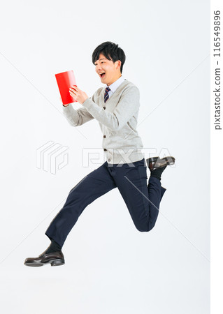 Full-body photo of a male student in uniform jumping while reading a red book Full-body photo of a male student in uniform jumping while reading a red book 116549896