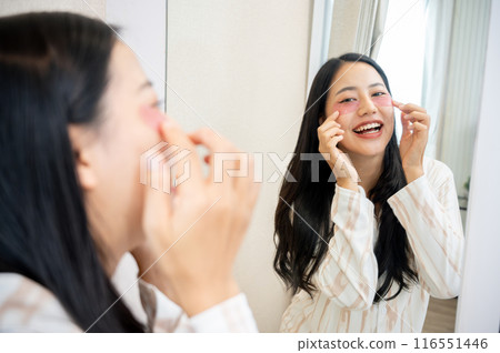 A beautiful Asian woman in pajamas is applying eye patches, doing her night skin care routine. A beautiful Asian woman in pajamas is applying eye patches, doing her night skin care routine. 116551446