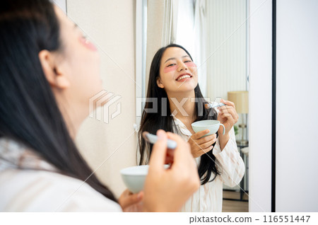 A beautiful Asian woman in pajamas is applying eye patches, doing her night skin care routine. 116551447
