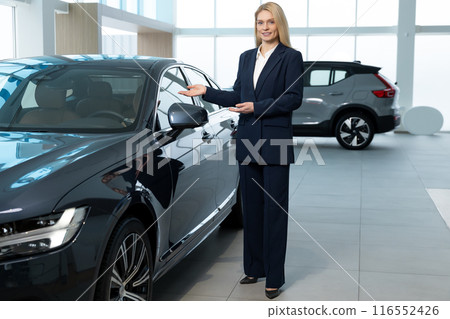 Woman in a black suit standing near the car in a showroom 116552426