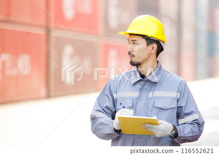 Asian male logistic worker in safety workwear portrait at the container yard. Logistic foreman portrait. Asian male logistic worker in safety workwear portrait at the container yard. Logistic foreman portrait. 116552621