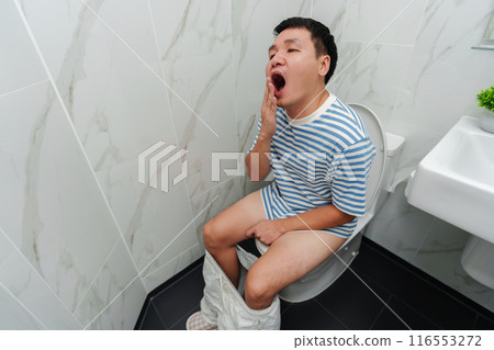 man sleepy and yawning while sitting on toilet bowl in bathroom 116553272