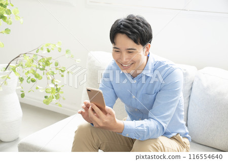 一個男人坐在沙發上，拿著智慧型手機 116554640