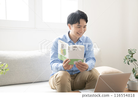 一個男人坐在沙發上讀投資書 一個男人坐在沙發上讀投資書 116554818