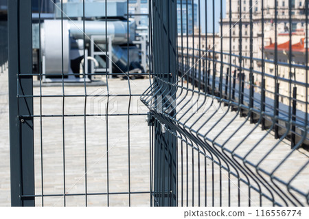 A close up of a metal fence with a building in the background on a city street A close up of a metal fence with a building in the background on a city street 116556774