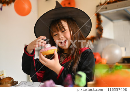 Cute little girl decorating Halloween dessert in the kitchen. People, holiday and festival concept 116557498