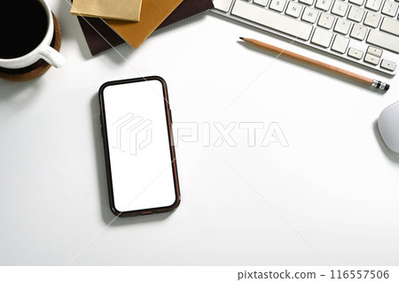 Top view a smartphone with blank screen, coffee cup and office supplies on white table 116557506