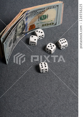 White dice with black markings. They lie on a surface covered with a coarse gray cloth. Nearby are a few dollar bills of different denominations. 116558225