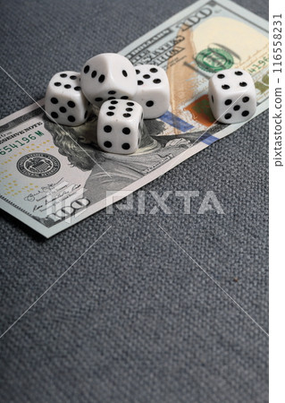 White dice with black markings. They lie on a surface covered with a coarse gray cloth. Under them lies a hundred dollar bill. 116558231