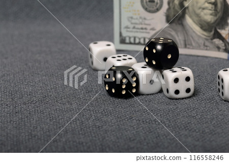 White dice with black markings. They lie on a surface covered with a coarse gray cloth. Among them are two black dice with white markings. Nearby is a hundred dollar bill. 116558246