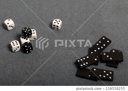 White dice with black markings. They lie on a surface covered with a coarse gray cloth. Among them are two black dice with white markings. Next door are dominoes. 116558255