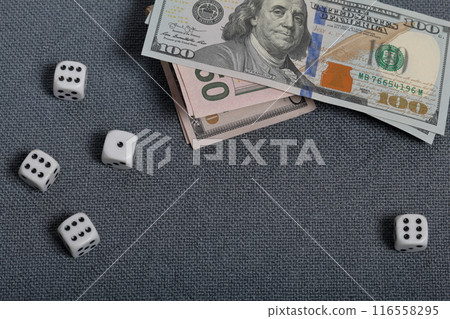 White dice with black markings. They lie on a surface covered with a coarse gray cloth. Nearby are a few dollar bills of different denominations. 116558295