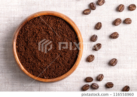 Coffee powder, freshly ground coffee beans in a wooden bowl on linen fabric. On the right roasted seeds of berries from Coffea arabica, also Arabian, mountain or arabica coffee. Close-up, from above. 116558960