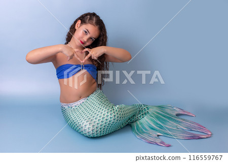 A beautiful child girl in a mermaid costume, sitting on a blue background A beautiful child girl in a mermaid costume, sitting on a blue background 116559767