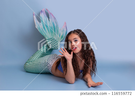 Charming girl in a mermaid costume, friendly, lies isolated on a blue background Charming girl in a mermaid costume, friendly, lies isolated on a blue background 116559772