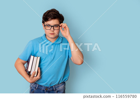 A cute schoolboy in glasses and a blue T-shirt, holding a stack of books A cute schoolboy in glasses and a blue T-shirt, holding a stack of books 116559780